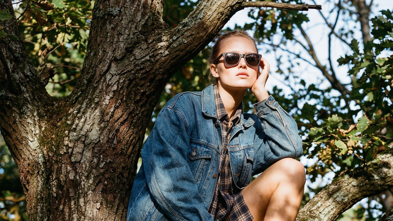 Woman in denim jacket and sunglasses sitting under a tree